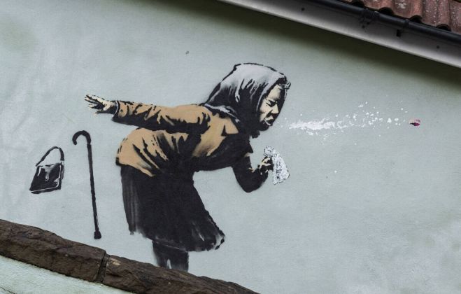 Banksy: Η τελευταία τοιχογραφία του πιο διάσημου παγκοσμίως street artist, σχολιάζει για άλλη μια φορά σκωπτικά την πρωτοφανή πανδημία τοου κορωνοϊού. Ο Banksy ζωγραφίζει μία γηραιά κυρία να χάνει μέχρι και τη μασέλα της ενώ τραντάζεται ολόκληρη από το φτέρνισμα. 